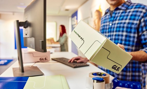 GLS työntekijä pitää kädessään GLS-logolla varustettua pakettia GLS noutopist
