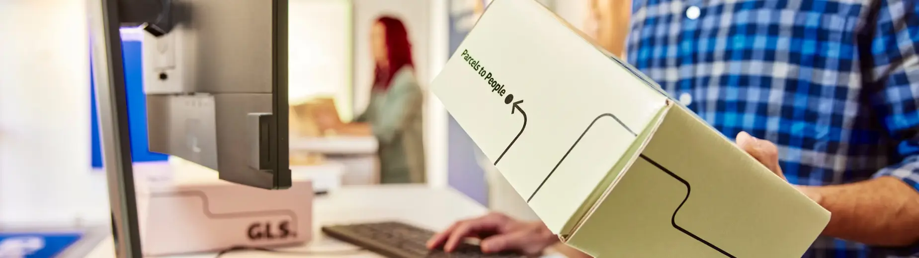 Close-up of a customer handing over a GLS parcel at a shipping counter, highlighting a shipping solution for professionals.