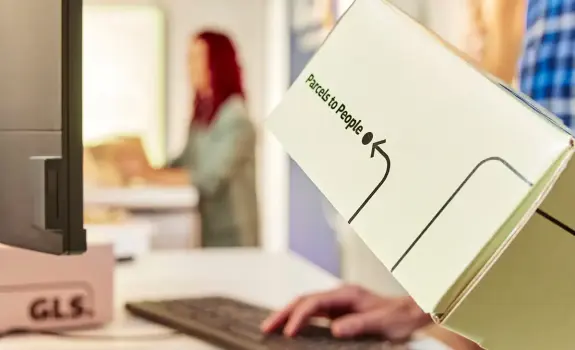 Close-up of a customer handing over a GLS parcel at a shipping counter, highlighting a shipping solution for professionals.